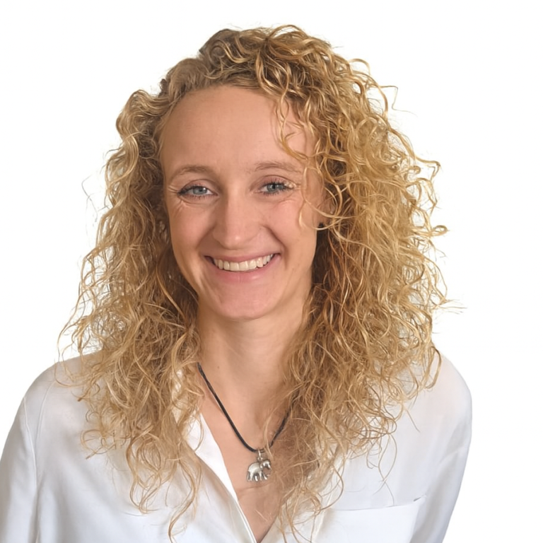 Lächelnde Frau mit lockigem, blondem Haar, trägt ein weißes Hemd.